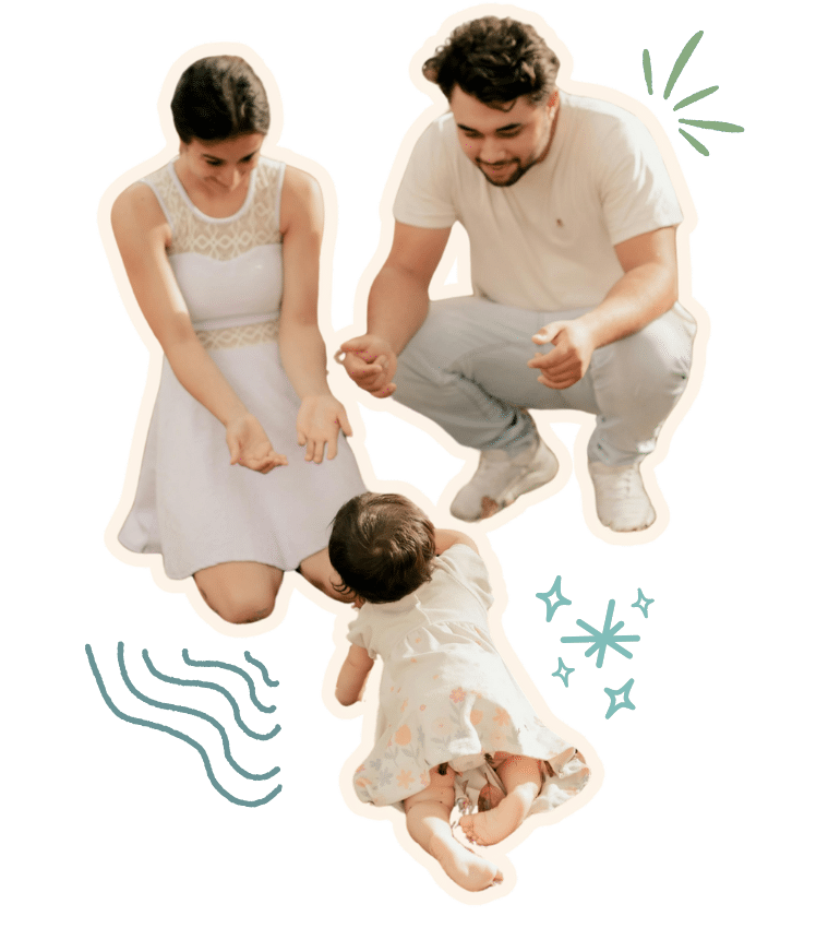 A young woman and man kneeling down with open arms as their baby crawls towards them
