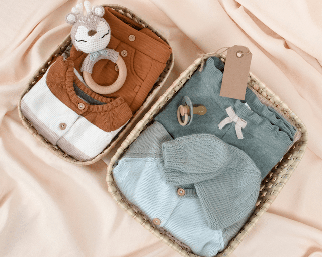 Two baskets full of baby clothes and items, one basket has brown items and the other has blue items